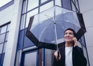 a trader woman on the phone smiling protected by an umbrella as a metaphore to trade while protecting your investment